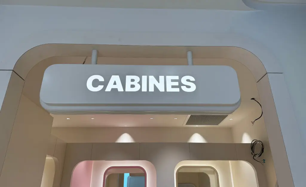 Enseigne lumineuse « CABINES » installée au-dessus d’un espace de cabines, avec lettrage blanc sur fond bleu.