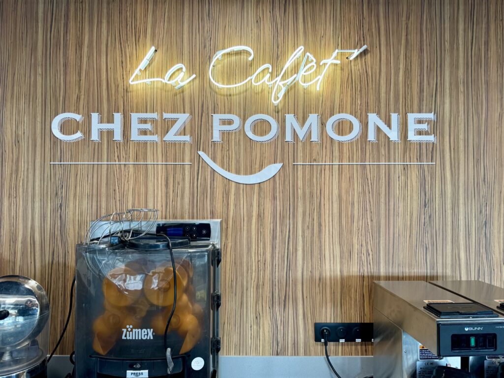 Signalétique murale "La Cafét Chez Pomone" avec écriture néon en verre soufflé et lettres en plexiglas blanc sur fond bois, réalisée par CYGN & LUMEN.