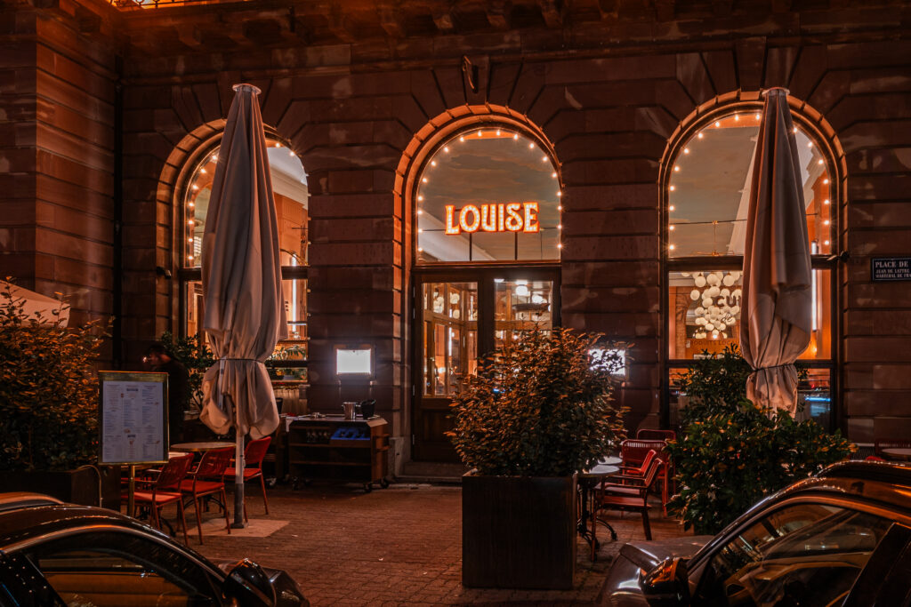 Façade principale de la Brasserie Louise à Strasbourg avec enseigne en lettres baignoire à ampoules et soulignement lumineux des arches vitrées.