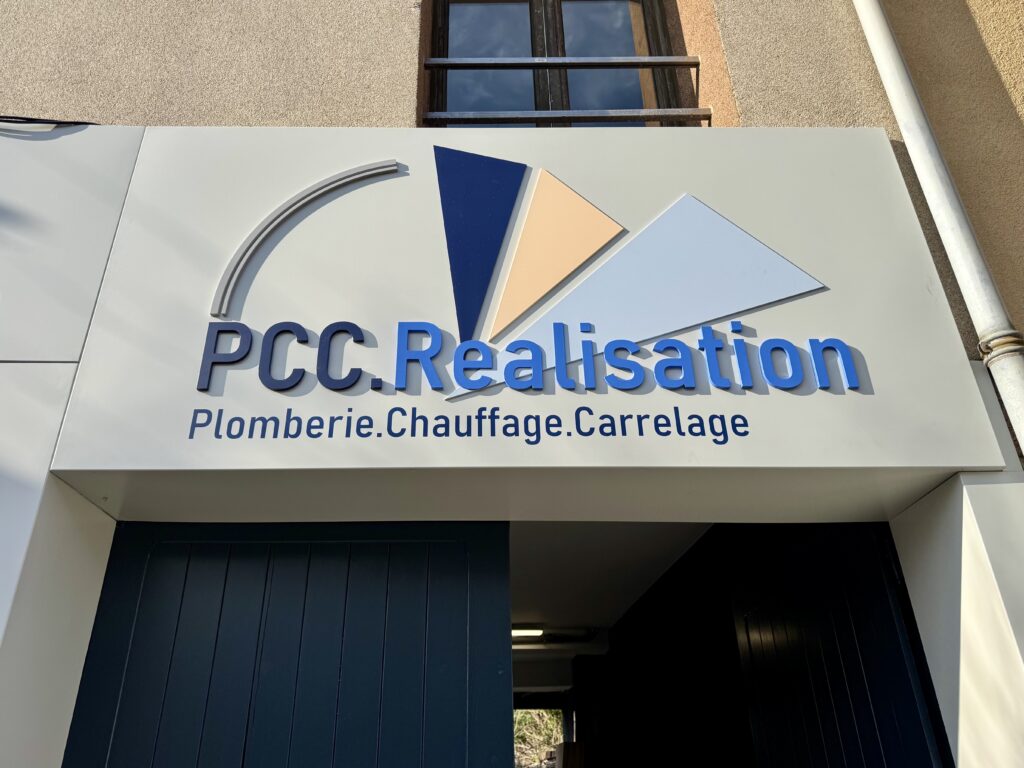 Enseigne commerciale de PCC.Réalisation installée sur façade, conçue par CYGN & LUMEN. Logo en relief 3D, textes "PCC.Réalisation" et "Plomberie.Chauffage.Carrelage".