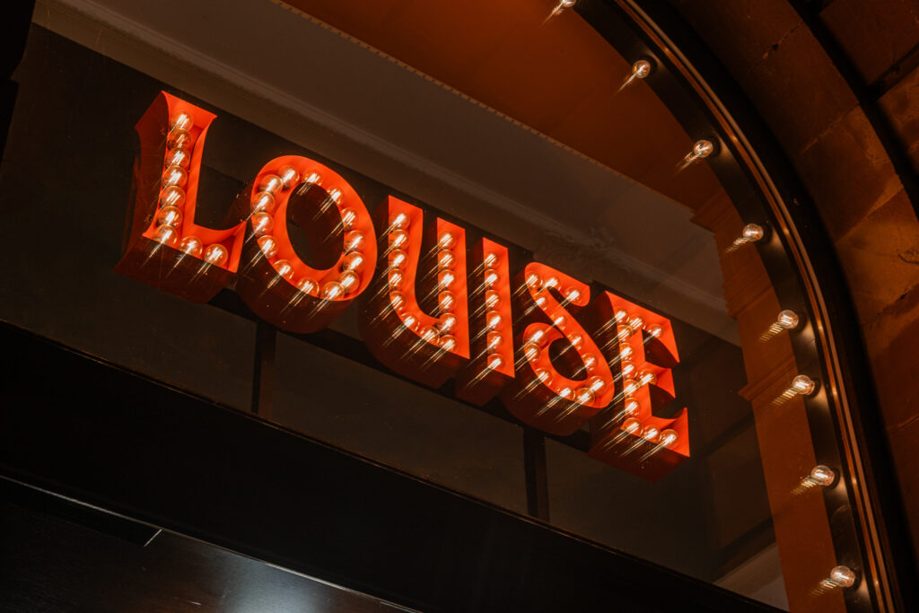 Gros plan sur l’enseigne LOUISE de la Brasserie Louise à Strasbourg avec lettres baignoires et ampoules à filament.