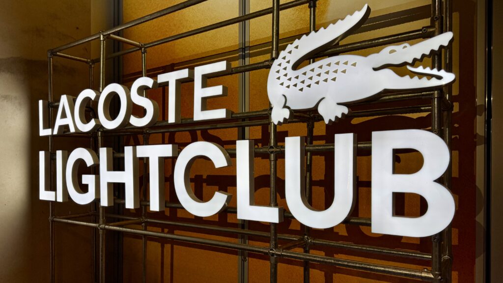 Détail de l’enseigne lumineuse Lacoste Lightclub en lettres boîtiers, fixée sur un échafaudage.