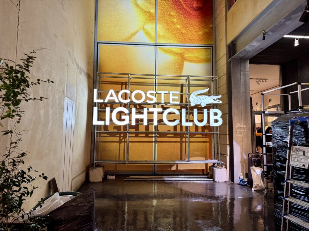 Enseigne lumineuse LACOSTE LIGHTCLUB à Paris avec lettres néon LED blanches et logo crocodile sur structure métallique.