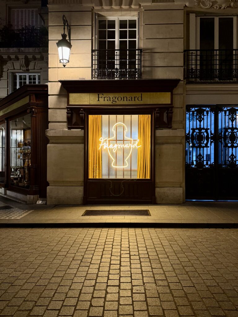 Façade nocturne du musée du parfum Fragonard à Paris avec une enseigne lumineuse néon en vitrine représentant un flacon de parfum et un lettrage manuscrit.