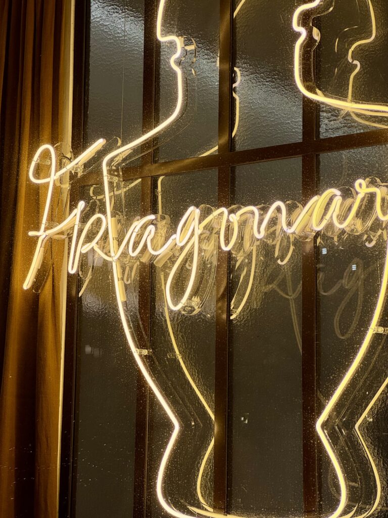 Vue en contre-plongée de la vitrine du Musée du Parfum Fragonard à Paris avec lettrage or "Fragonard" et enseigne néon en forme de flacon.