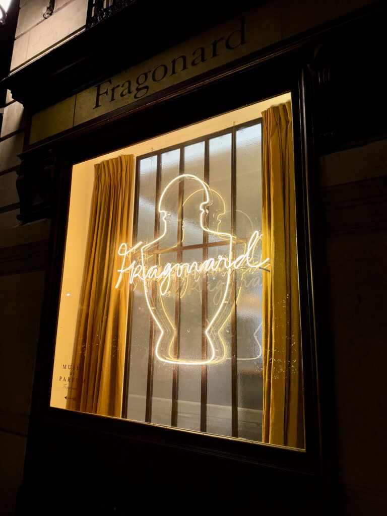 Vitrine nocturne du Musée du Parfum Fragonard à Paris avec enseigne lumineuse verre soufflé blanc chaud en forme de flacon et signature manuscrite.