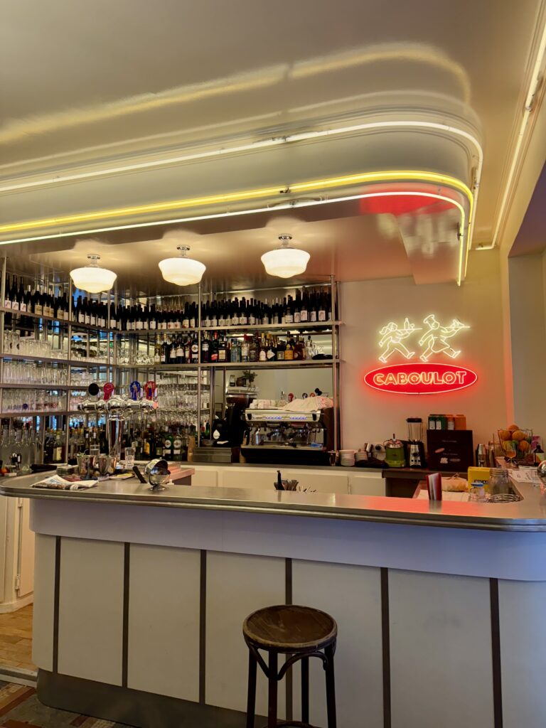 Vue intérieure du comptoir de la Brasserie Caboulot à Paris dans le 18ème avec une enseigne en néon en verre rouge et blanc et un éclairage indirect en corniche.