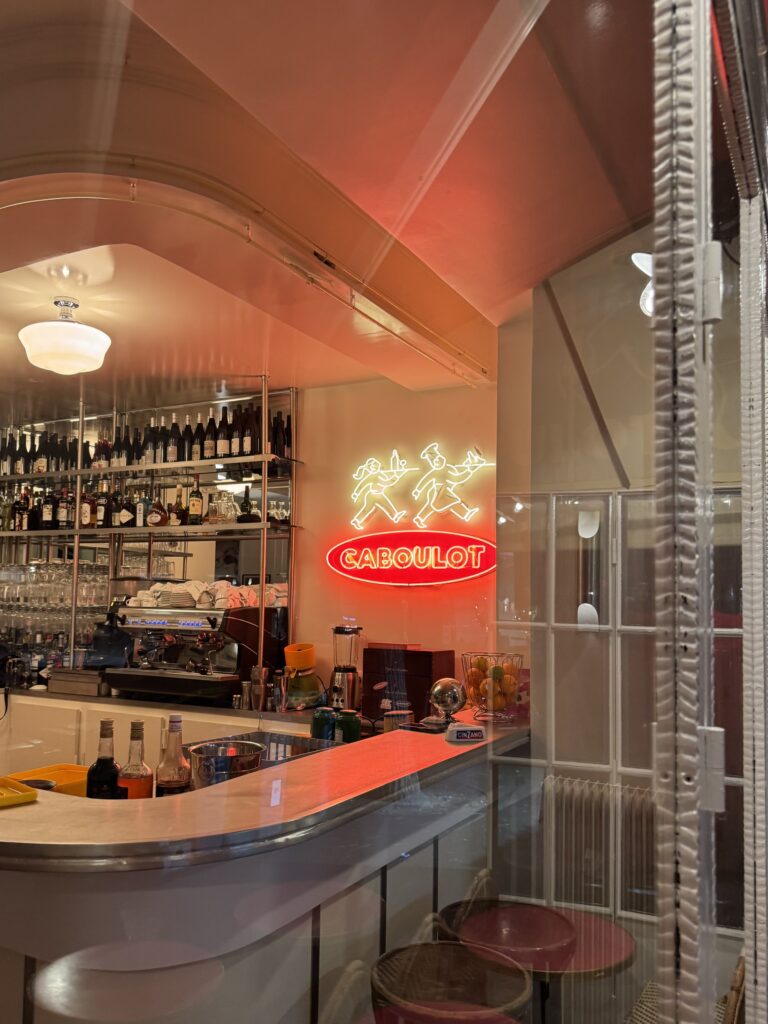 Vue à travers la vitrine du bar de la Brasserie Caboulot à Paris 18ème avec son enseigne lumineuse en néon verre rouge et blanc.