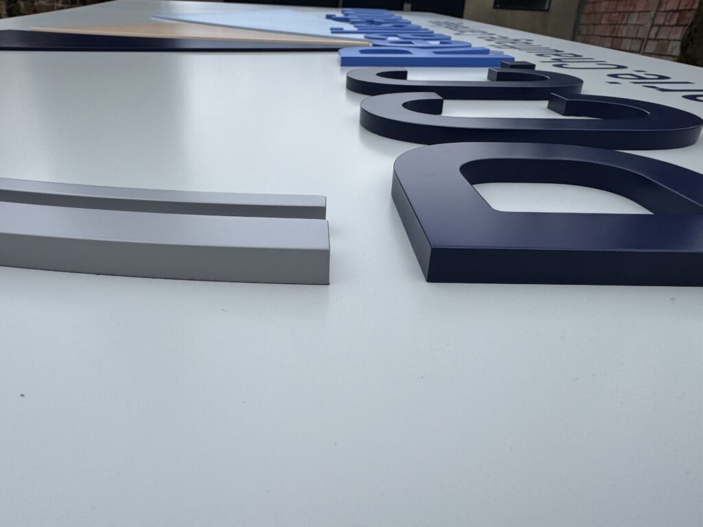 Gros plan en angle sur les lettres en relief 3D (dont la lettre 'D') et les profilés de précision en tôles peintes pour l'enseigne de PCC.Réalisation, par CYGN & LUMEN.